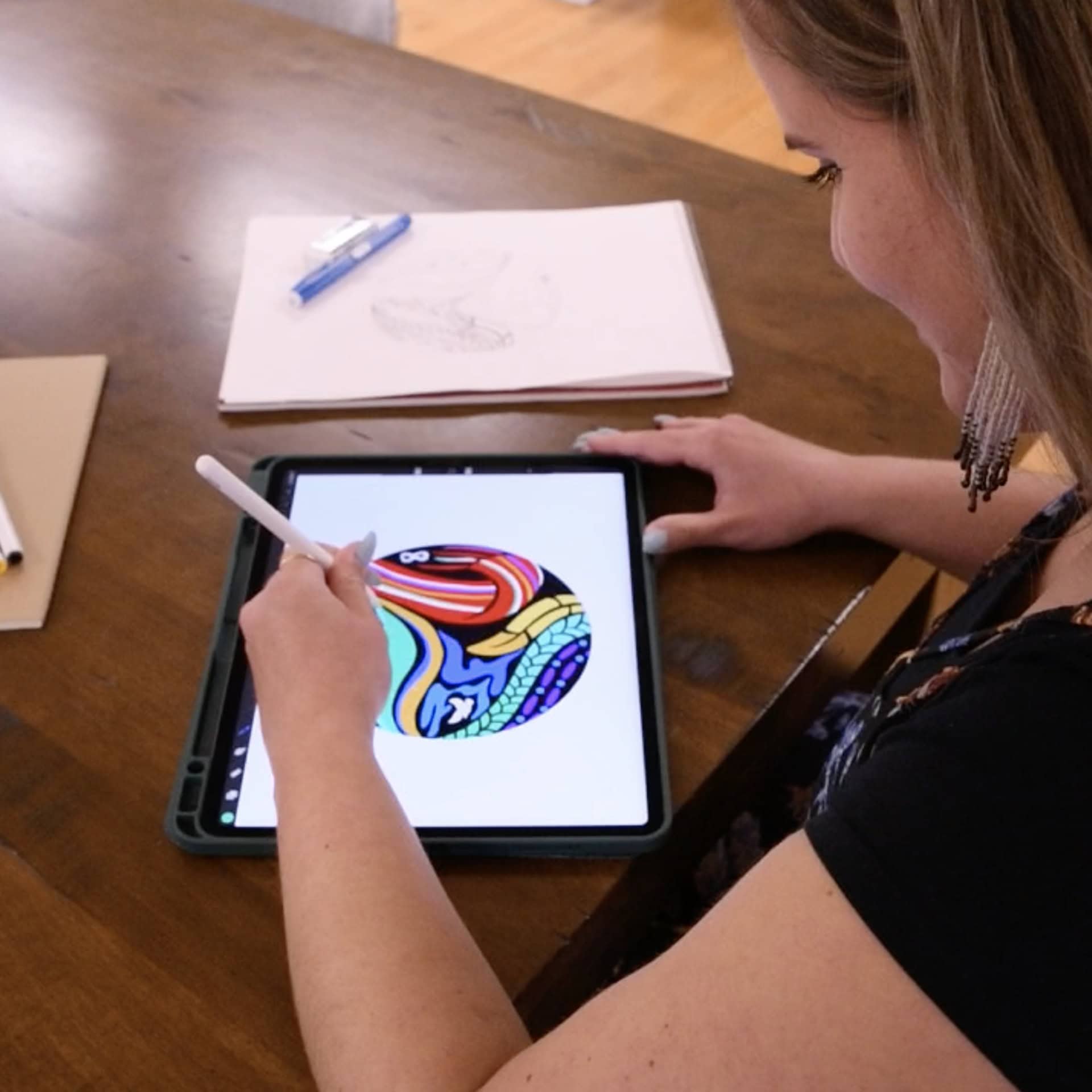Jennica sketching CBC logo graphics on a tablet seated in the office.