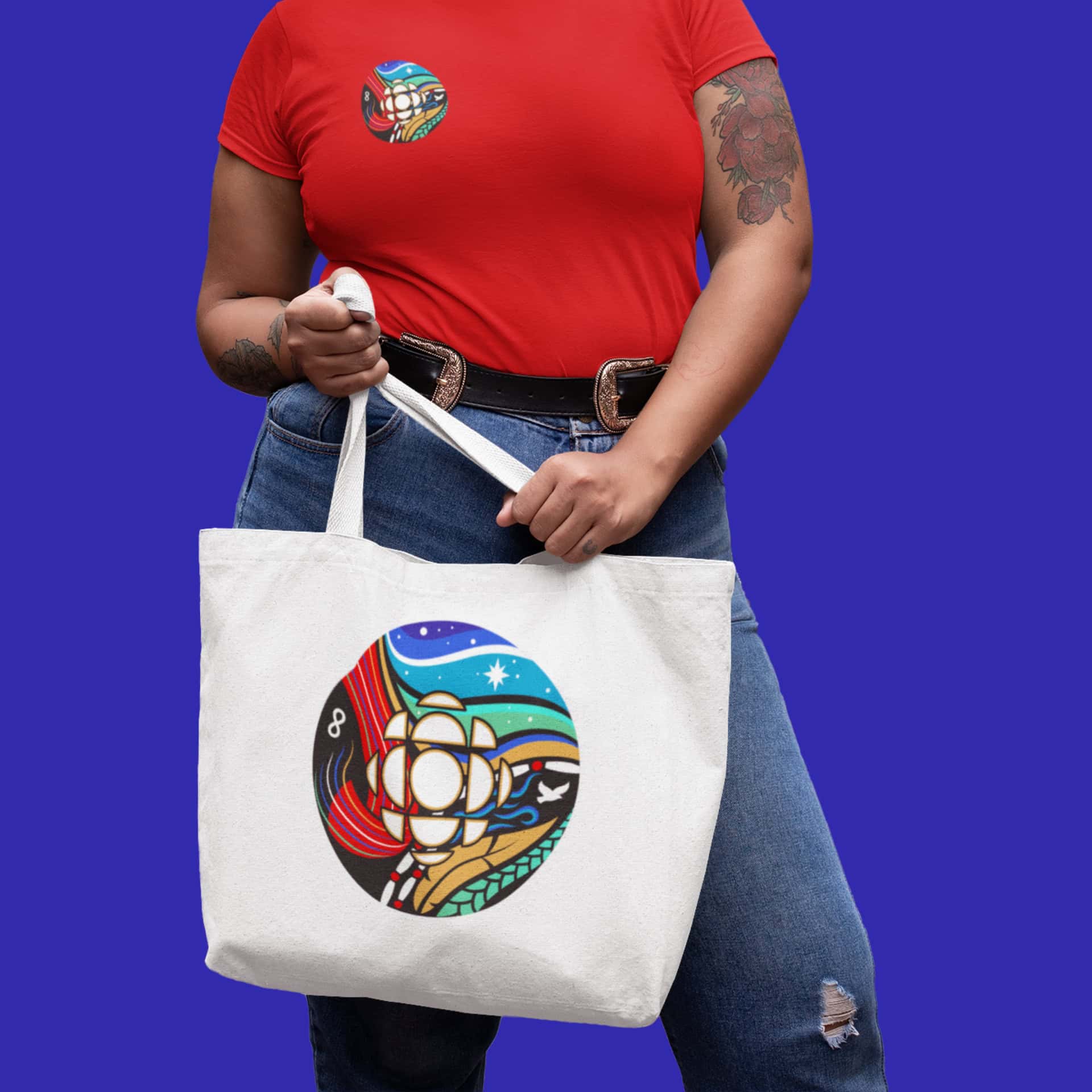 A woman wearing a red shirt and jeans is holding a tote. On her t-shirt and on the tote are displayed the CBC 'gem' designed by DDP