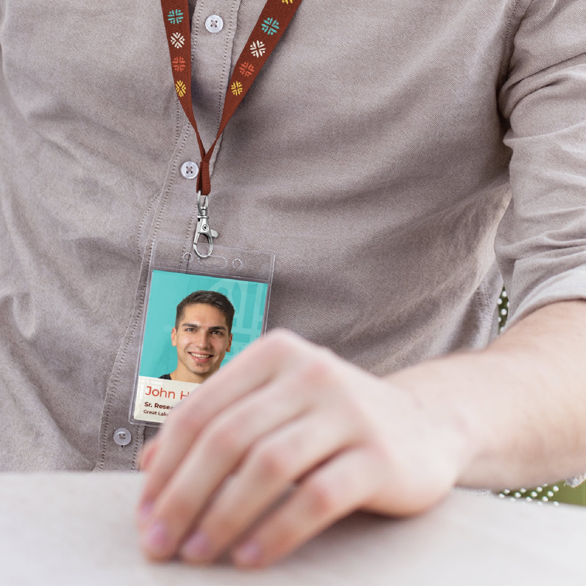 We see a zoomed in shot of a man's chest and arm resting on a table. There is a lanyard hanging from his neck; the name tag with the Center's branding can be seen with the man's accompanying headshot.