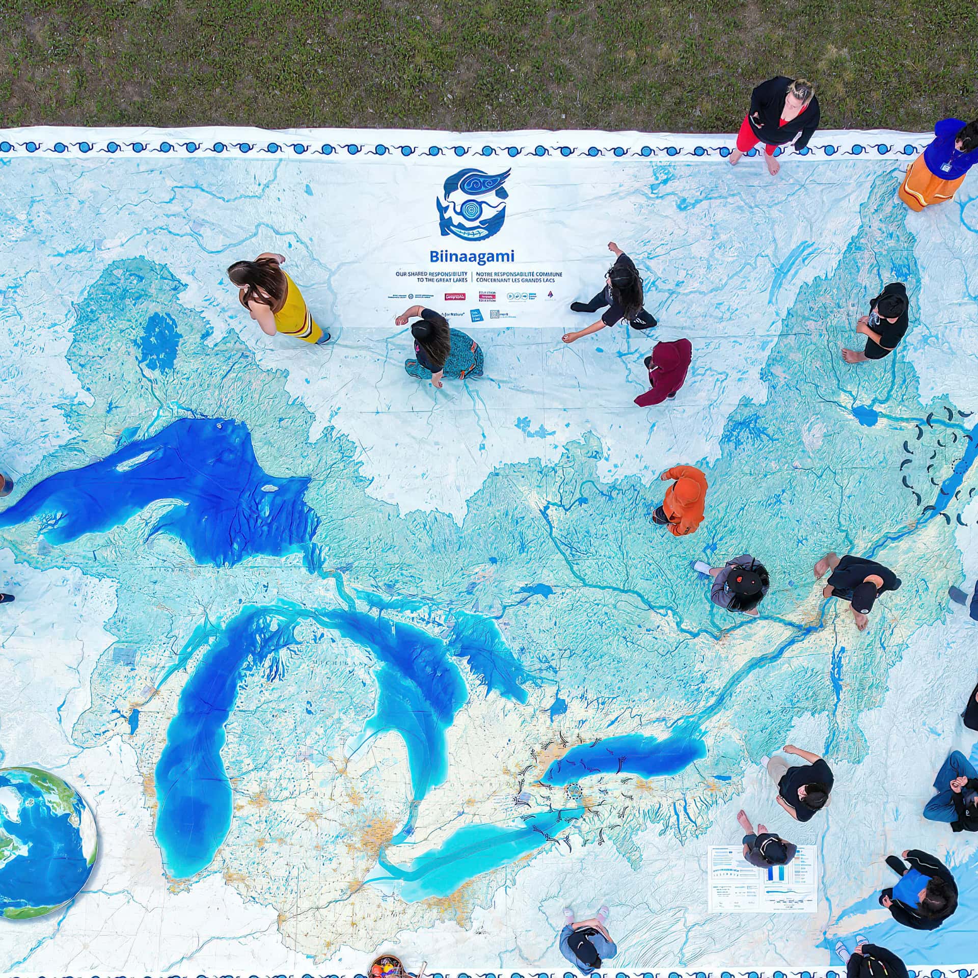 An overhead shot looking down at people walking over a large map of the Great Lakes covering the floor. The Biinaagami logo is displayed at the top of the map.