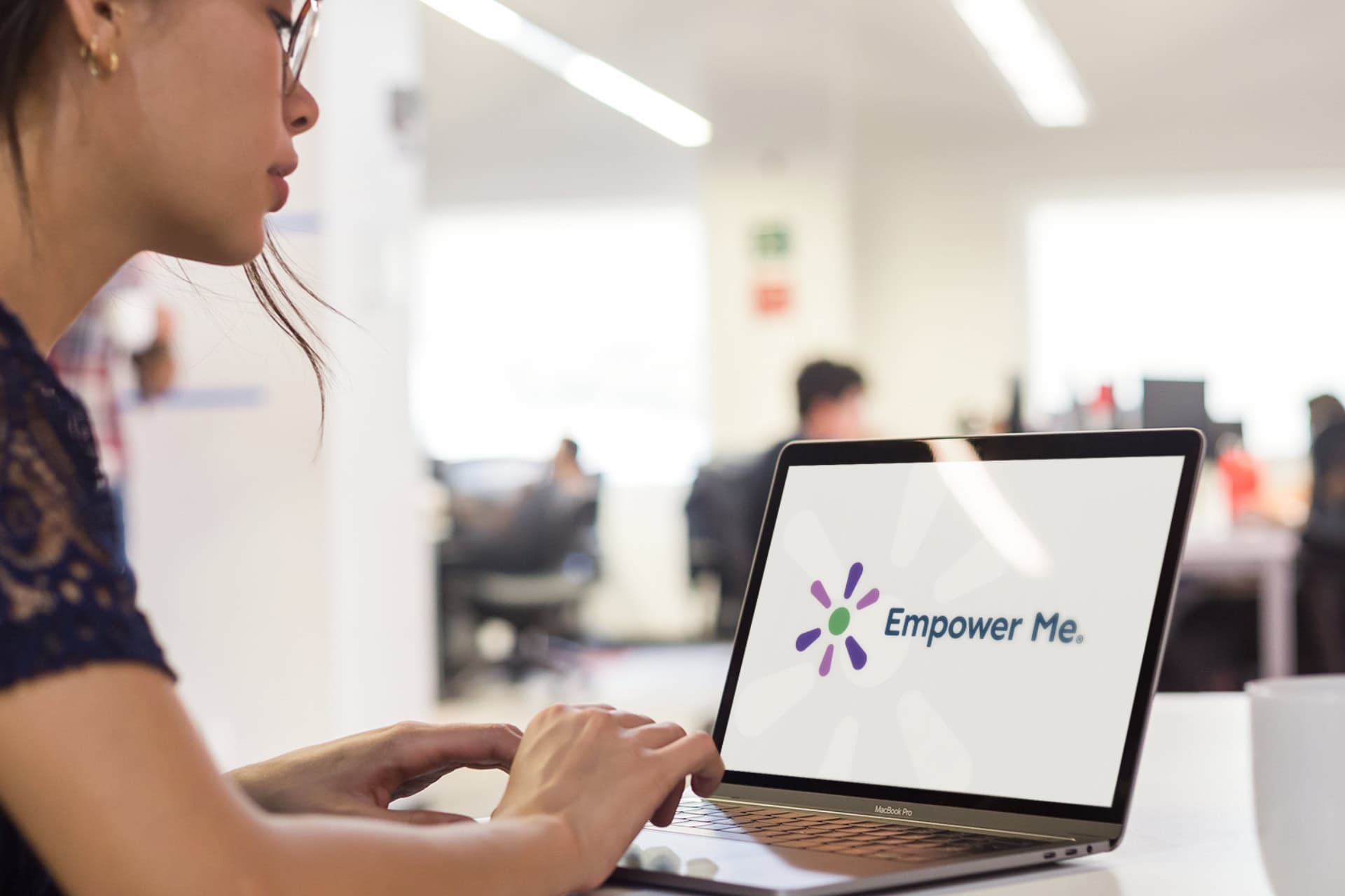 A woman looks at a mockup of a logo on her laptop. The logo text reads 'Empower Me' in brand colours.