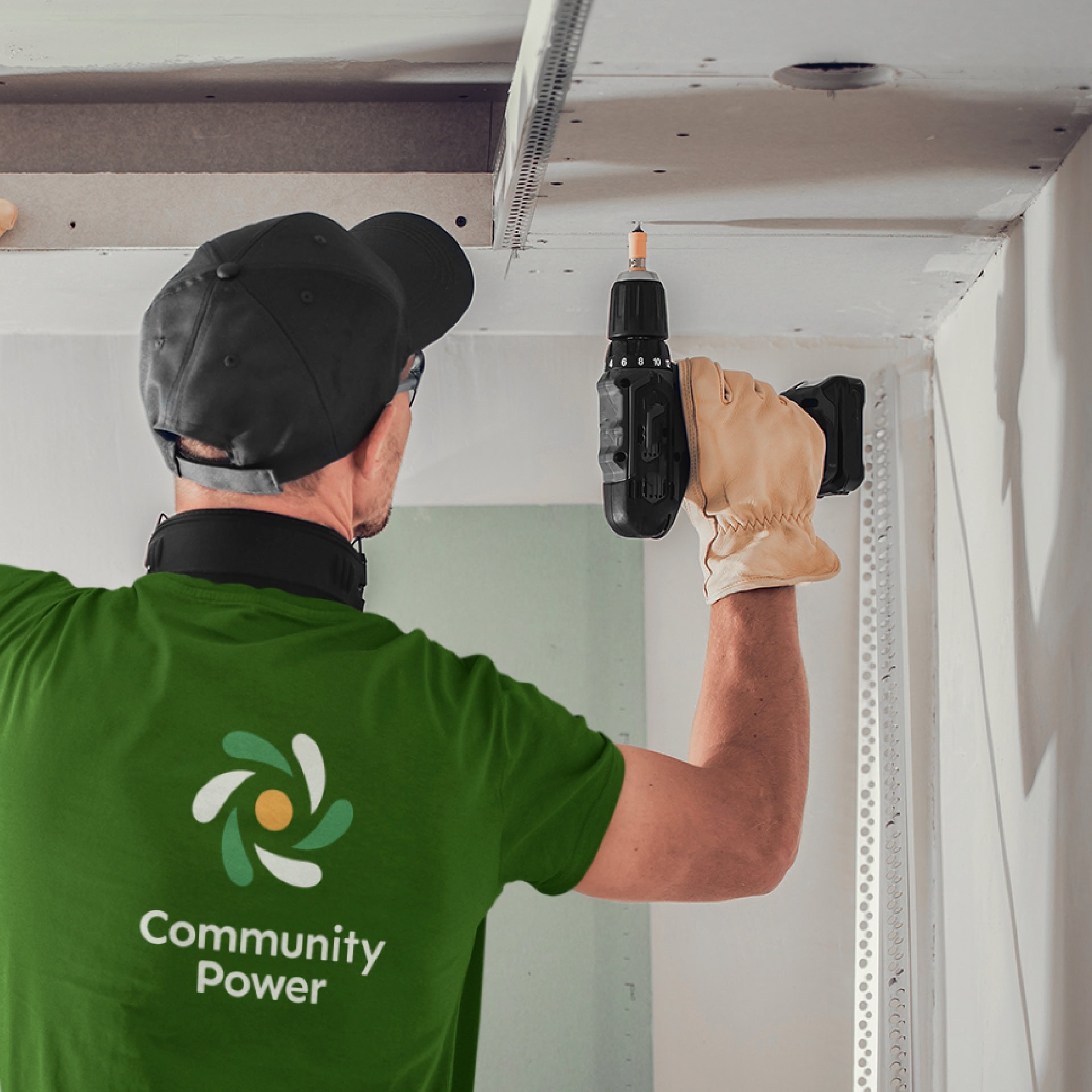 A man in a green shirt with the Kambo 'Community Power' logo on it drills into an attic wall where energy improvement work is ongoing.