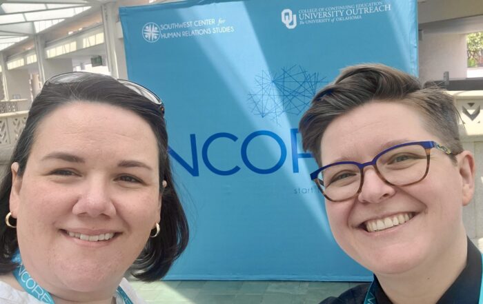 DDP’s Co-CEOs Jennifer Taback and Meggan Van Harten stand in front of a conference sign stating the name of the conference, NCORE.