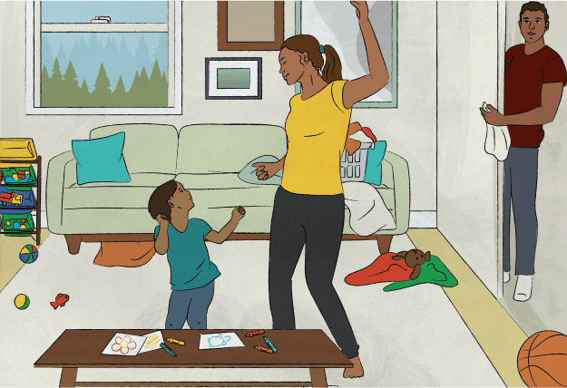 A mother and son dance excitedly in a lived-in living room while the father looks in with happiness.