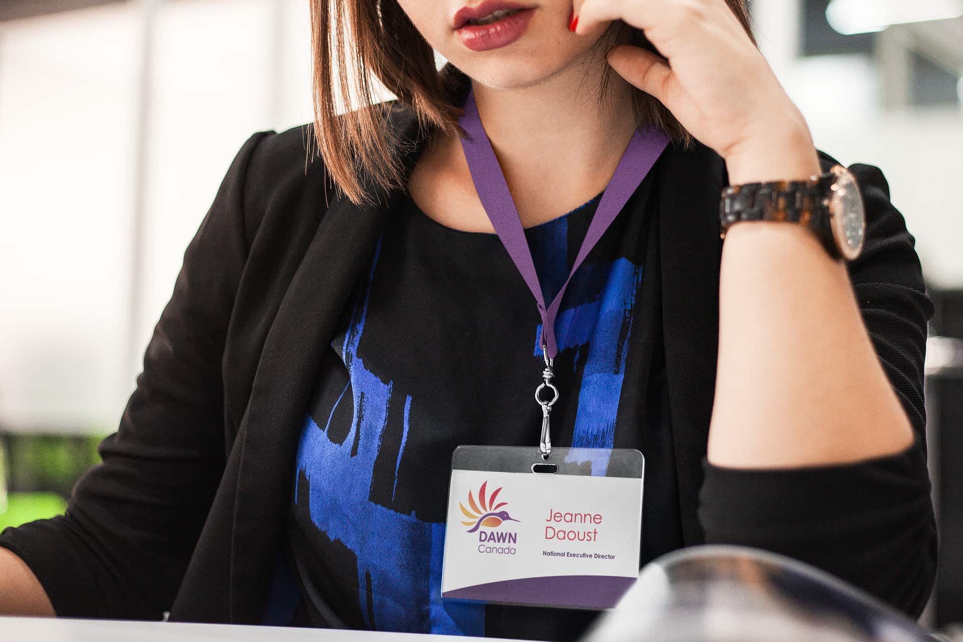 A business professional wearing a dark purple lanyard with a name badge attached that reads "Jeanne Daoust, National Executive Director" and features the DAWN Canada logo.