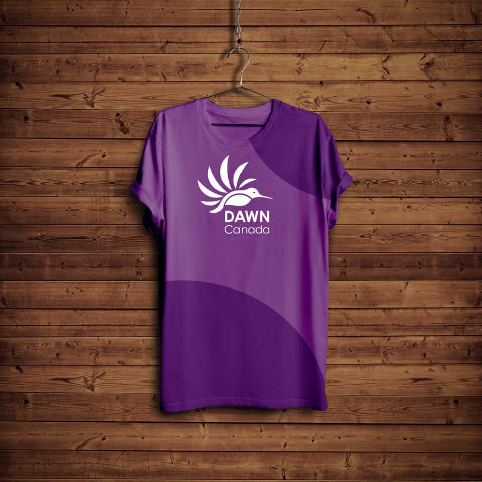 A dark purple t-shirt hanging on a metal clothes hanger in front of a wood-lined wall. The t-shirt has a white DAWN Canada logo on the front.