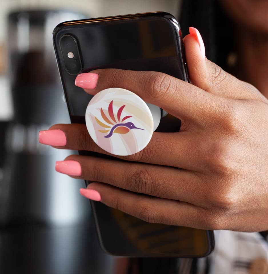 Hand with long pink nails holding a cell phone with a white pop socket on the back that features the DAWN Canada logo.