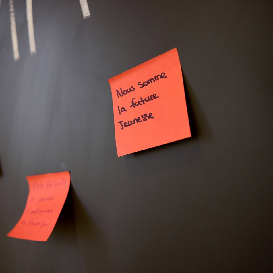 An orange post-it note stuck to a clean chalk board reads "Nous somme la future Jeunesse".