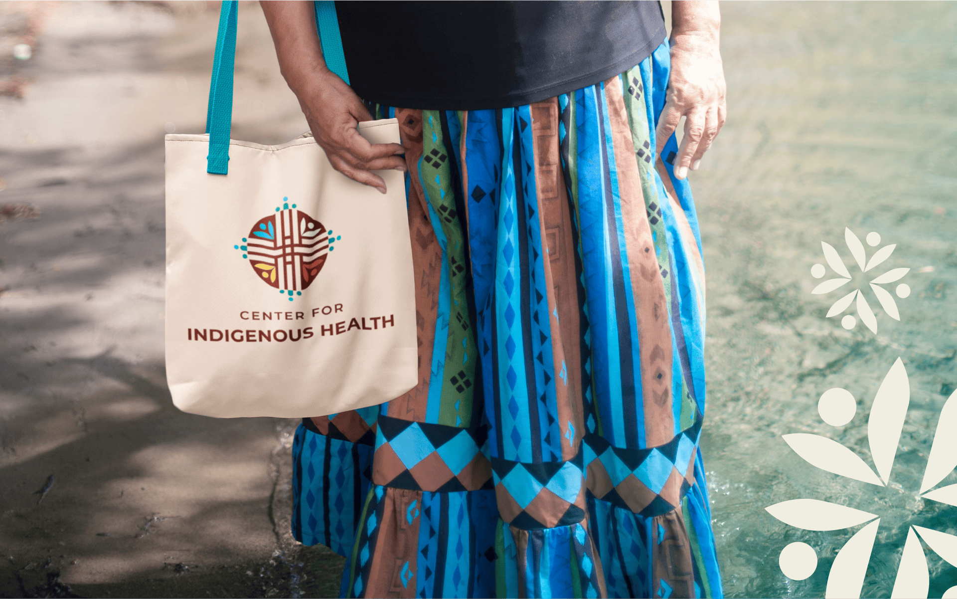 Indigenous woman wearing a colourful long skirt and holding a tote bag with the Center for Indigenous Health logo on it.