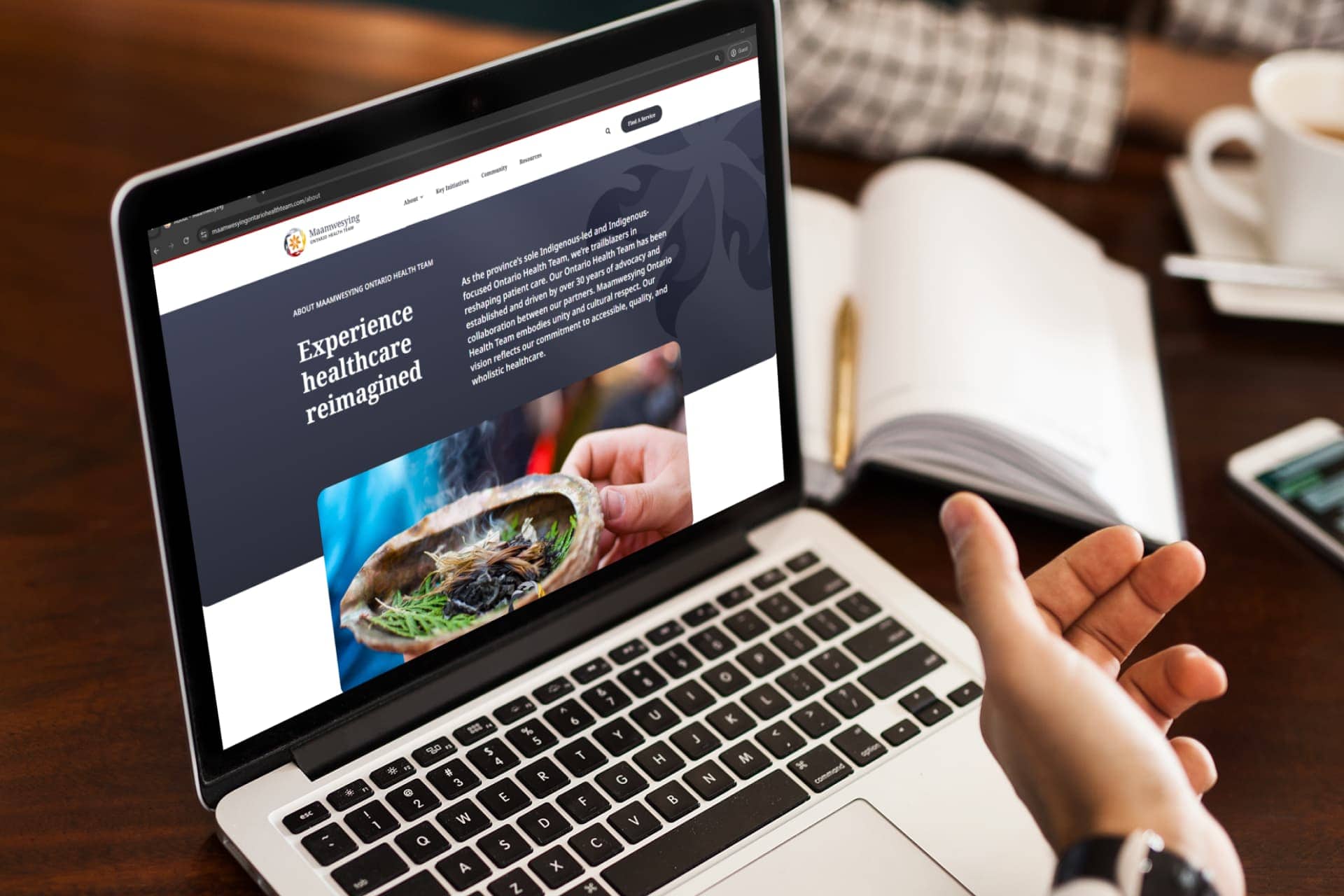 A laptop on a large desk in front of a healthcare professional speaking to a patient. The laptop displays the Maamwesying website. On the website is a description of what an Ontario health team is.