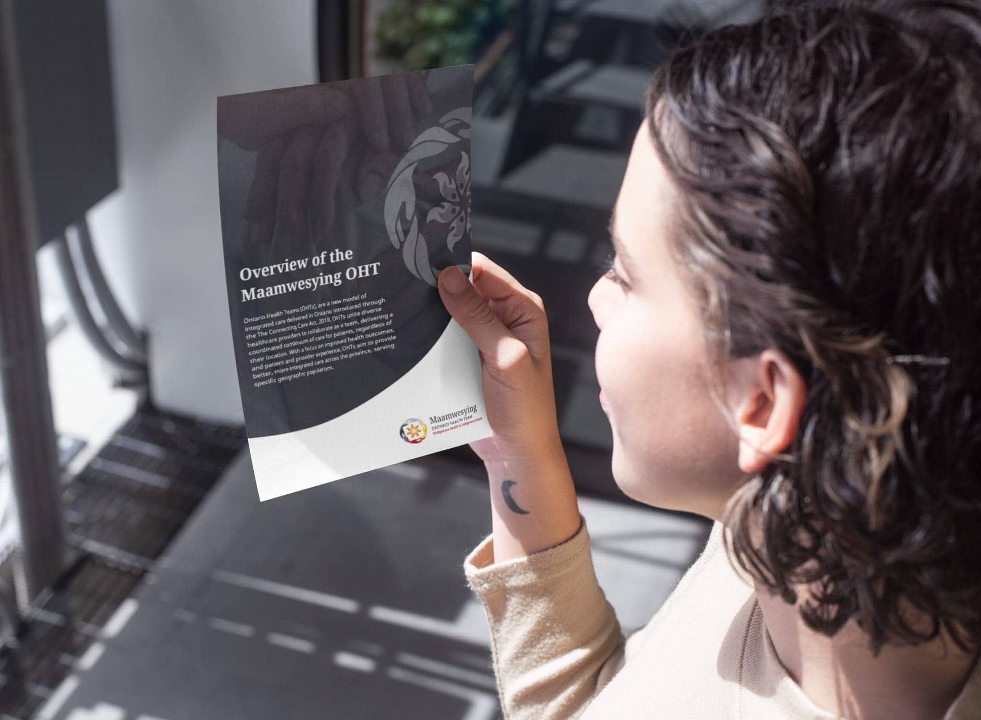 Young dark-haired woman in a professional environment holding up a flying that says "Overview of the Maamwesying OHT"