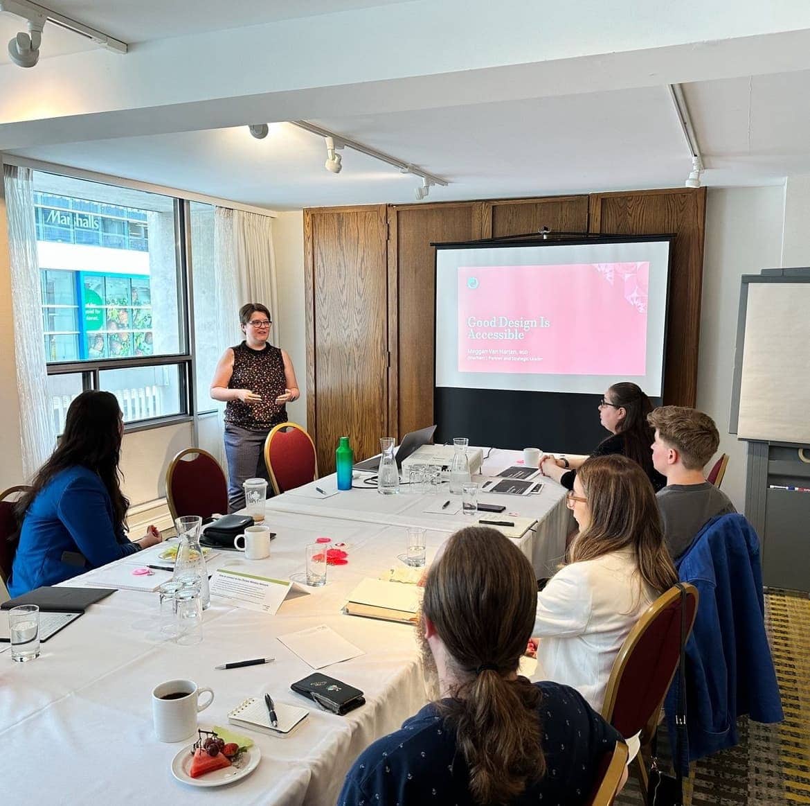 22406b7fac7be55d6c1659d391c6a41f9d4fdfc5 (1) Meggan Van Harten presenting a workshop to a small group in an office conference room.